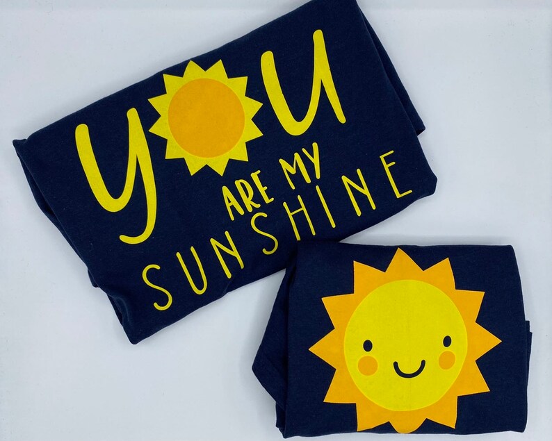 May include: Two navy blue t-shirts with yellow sun designs and the text "You are my sunshine".