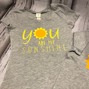 May include: A grey t-shirt with a yellow sun and the text "You are my sunshine" printed on the front.