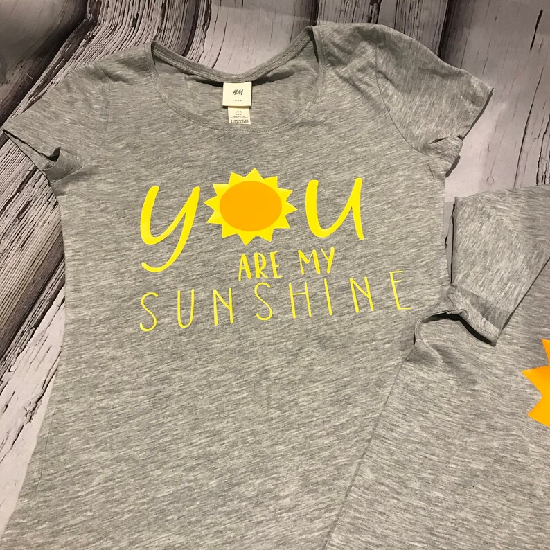 May include: A grey t-shirt with a yellow sun and the text "You are my sunshine" printed on the front.