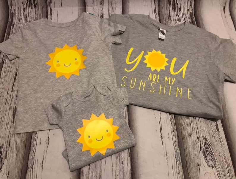 May include: Three grey t-shirts with a yellow sun graphic. The largest shirt says "You are my sunshine" with a yellow sun graphic.
