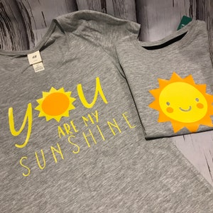 May include: Two grey t-shirts with yellow sun designs. One shirt says "You are my sunshine".