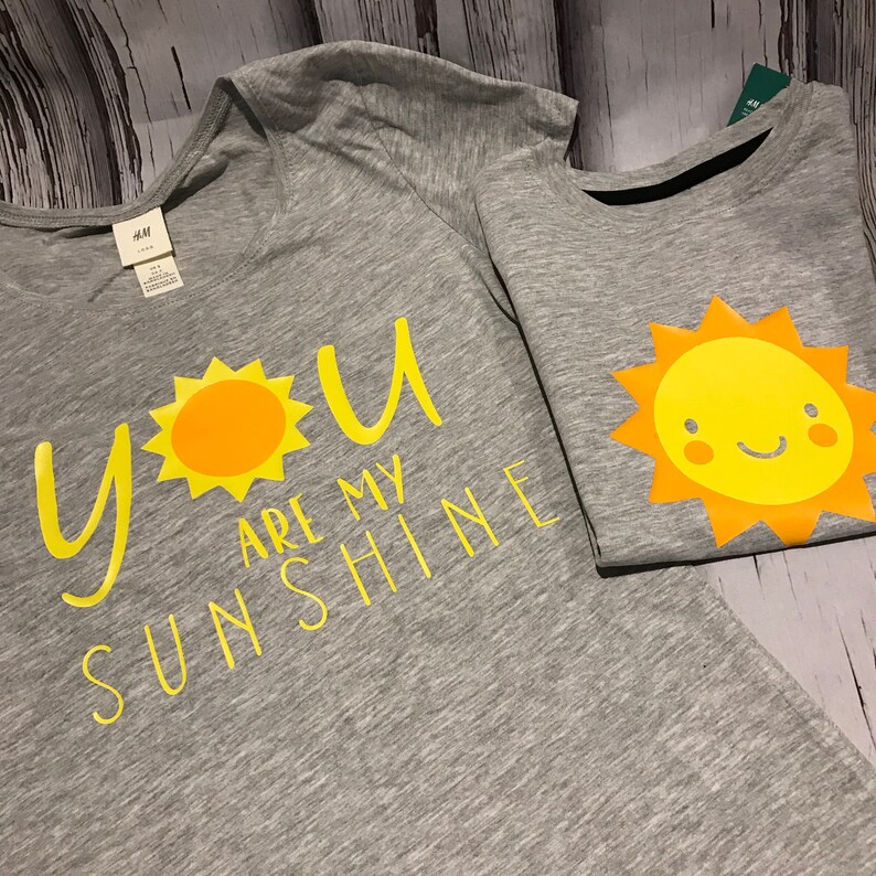 May include: Two grey t-shirts with yellow sun designs. One shirt says "You are my sunshine".