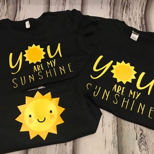May include: Two black t-shirts with the text "You are my sunshine" and a yellow sun graphic.