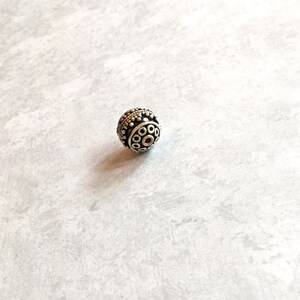 May include: A silver bead with a circular design featuring a series of small circles and a larger circle in the center.