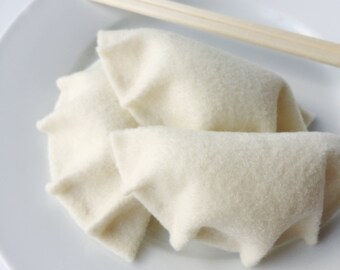 May include: Two white felt dumplings on a white plate with a wooden chopstick.