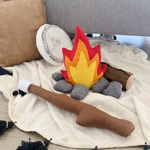 May include: A felt campfire play set with a red and yellow flame, brown logs, and gray rocks. The set is on a white blanket.