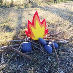May include: A felt fire pillow with a red and yellow flame design, surrounded by gray felt rocks on a bed of brown sticks.
