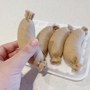 May include: Five brown felt sausages in a white plastic container. The sausages are arranged in a row, with the ends of the sausages facing the viewer.