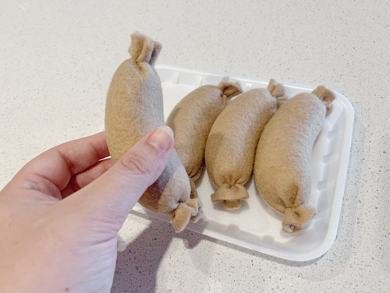 May include: Five brown felt sausages in a white plastic container. The sausages are arranged in a row, with the ends of the sausages facing the viewer.