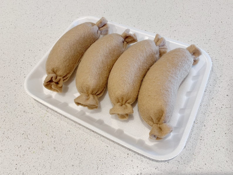May include: Four brown felt sausages in a white styrofoam tray. The sausages are arranged in a row, with the ends of each sausage facing the viewer.
