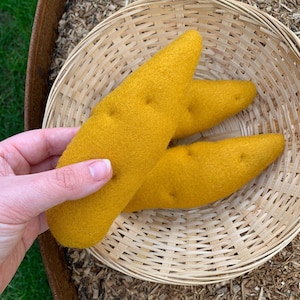May include: Two yellow felt sweet potatoes in a woven basket. The sweet potatoes are handmade and have a realistic texture.