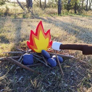 May include: A felt campfire set with a red and yellow flame, gray rocks, and a brown stick with a white marshmallow on the end.