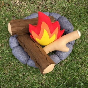May include: A felt campfire play set with two brown logs, a yellow and orange flame, and a gray rock fire pit.