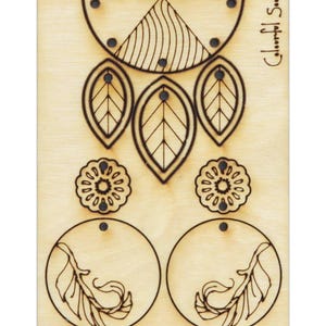 Könnte beinhalten: Eine Holzplatte mit Laser-geschnittenen Designs für Ohrringe. Die Platte enthält zwei Paar Ohrringe, ein Paar mit einem Blatt-Design und das andere mit einem Blumen-Design. Die Platte enthält auch ein Design für einen Anhänger mit einem Blatt und einem geometrischen Design.
