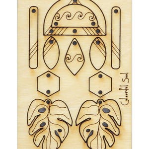 Könnte beinhalten: Eine Holzplatte mit Laser-geschnittenen Designs zum Herstellen von Ohrringen. Die Designs umfassen ein Paar tropischer Blätter, zwei Paare geometrischer Formen und ein Paar Tropfenformen mit Wellenlinien. Die Platte enthält auch zwei lange rechteckige Stücke mit Streifen und ein gebogenes Stück mit Wellenlinien.