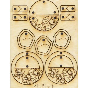 Könnte beinhalten: Eine Holzplatte mit Laser-geschnittenen Designs zum Herstellen von Ohrringen. Die Designs beinhalten zwei Halbkreise mit Blumenmustern, drei unregelmäßige Formen und zwei Paare kleiner Rechtecke. Der Text "Colorful Soul" ist am unteren Rand der Platte gedruckt.