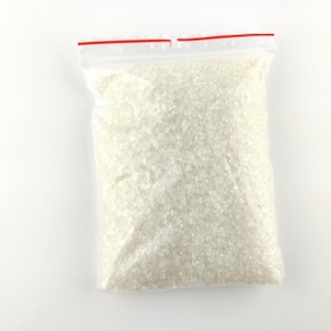 May include: A clear plastic bag filled with small, irregularly shaped, off-white crystals. The bag has a red zipper closure at the top and is set against a white background. The crystals appear to be a granular substance.