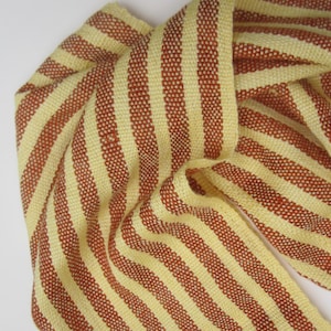 May include: A yellow and brown striped fabric with a woven texture. The fabric is folded and draped, showing the stripes.