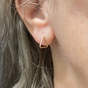 May include: A pair of gold triangle earrings. The earrings are simple and delicate, and they would make a great gift for a friend or loved one.