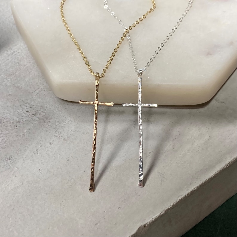 Pu&ograve; includere: Due delicate collane con croce in argento e oro con una texture martellata. Le collane sono esposte su una superficie bianca.