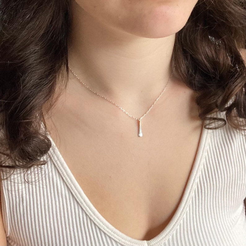 May include: A silver necklace with a delicate teardrop pendant. The necklace is worn by a person with long brown hair.