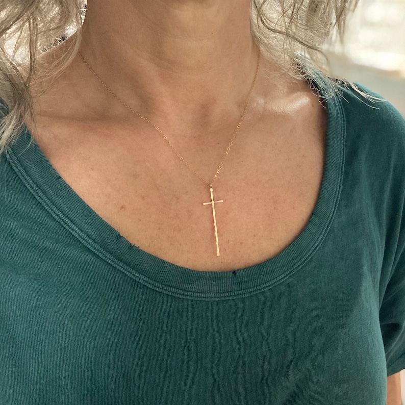 Pu&ograve; includere: Una collana con catena d'oro con un ciondolo a croce lungo, sottile e martellato.