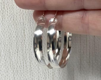 May include: A pair of silver hoop earrings with a hammered finish. The earrings are large and have a slightly curved shape.
