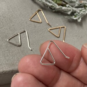 May include: A set of three triangle shaped earrings, two silver and one gold. The earrings are simple and minimalist in design.