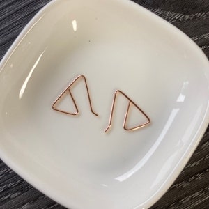May include: A pair of rose gold triangle earrings. The earrings are simple and delicate, and they would make a great gift for a friend or loved one.