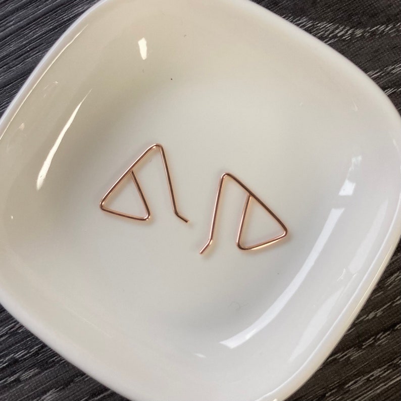May include: A pair of rose gold triangle earrings. The earrings are simple and delicate, and they would make a great gift for a friend or loved one.
