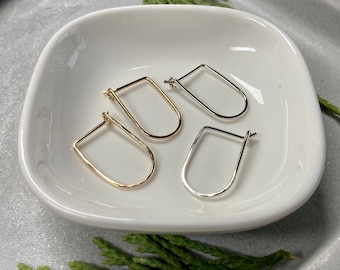 May include: Three pairs of hoop earrings in a white ceramic dish. Two pairs are gold and one pair is silver. The earrings are all in the shape of a teardrop.