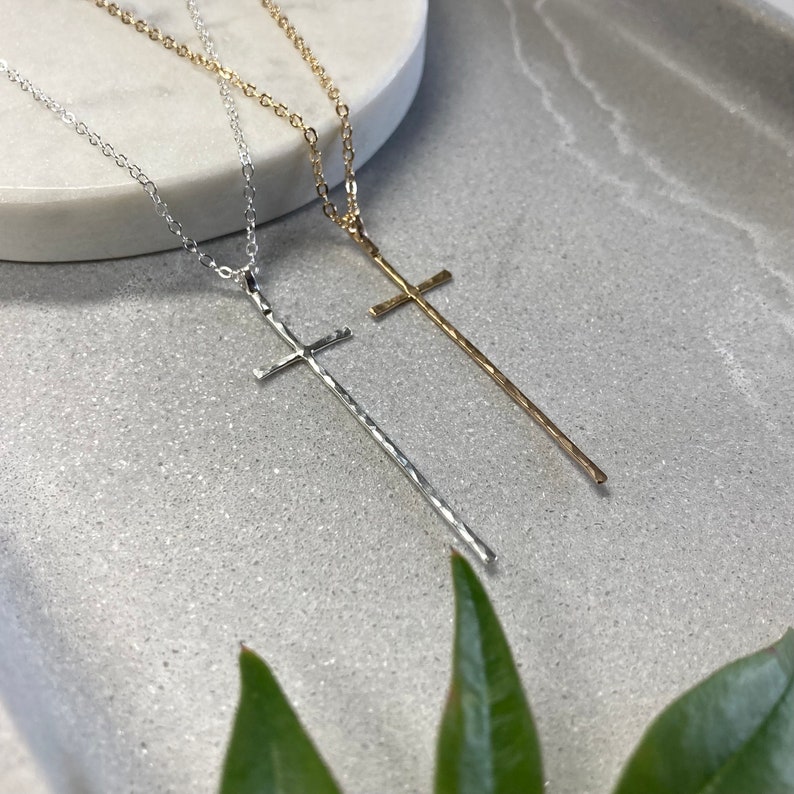 Pu&ograve; includere: Due delicate collane con lunghi ciondoli a croce martellati. Una collana &egrave; d'argento e l'altra &egrave; d'oro.