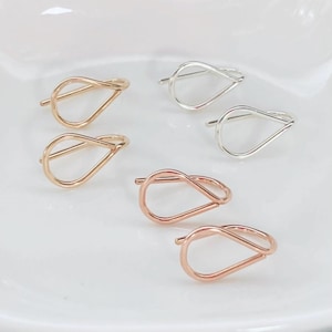May include: An assortment of six metal hair pins in gold, silver, and rose gold. The pins are shaped like a teardrop with a loop at the top. The pins are displayed on a white surface.