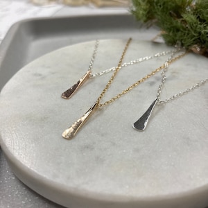 May include: Three delicate necklaces with a simple, hammered, teardrop-shaped pendant. The necklaces are silver, gold, and rose gold.