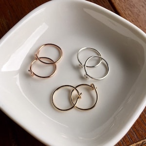 May include: Three pairs of hoop earrings in different metal finishes: gold, rose gold, and silver. The earrings are displayed on a white ceramic dish.