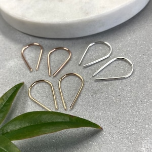 May include: Three pairs of teardrop-shaped earrings in gold, rose gold, and silver. The earrings are made of thin wire and have a simple, minimalist design.