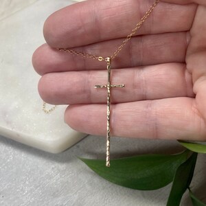 Pu&ograve; includere: Una collana con catena d'oro con un ciondolo a forma di croce lunga e martellata.