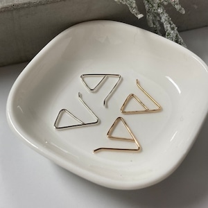 May include: Four triangle-shaped earring hooks, two gold and two silver, displayed on a white ceramic dish.