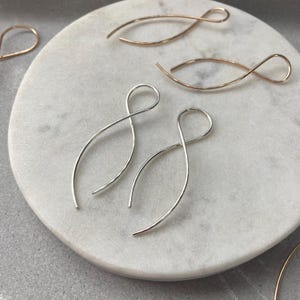 May include: A collection of minimalist earrings featuring a continuous wire loop design that forms an infinity or figure-eight shape. The set includes both silver-toned and rose gold-toned metal earrings, each with a smooth, polished finish.