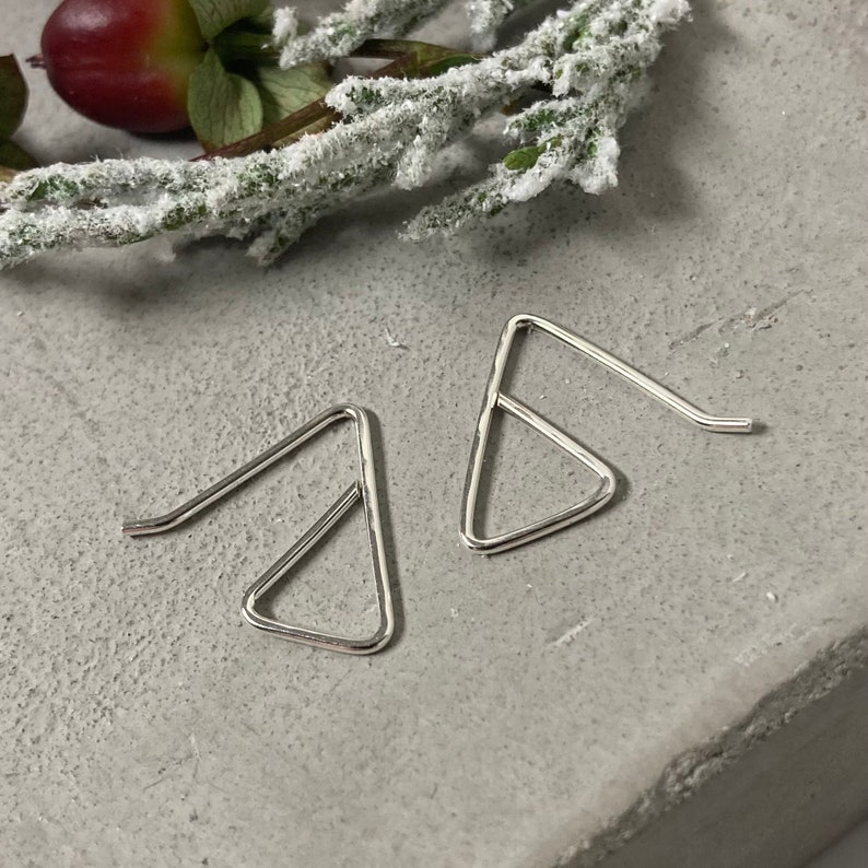 May include: A pair of silver triangle shaped earrings with a simple design.