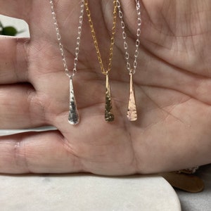 May include: Three delicate necklaces with hammered teardrop pendants. The necklaces are silver, gold, and rose gold.