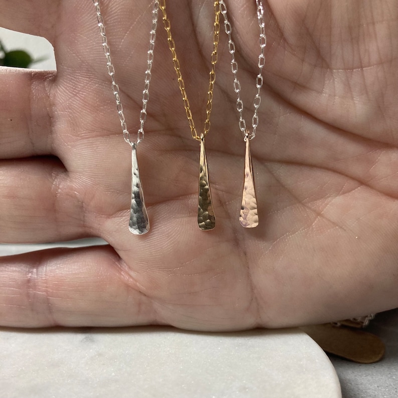 May include: Three delicate necklaces with hammered teardrop pendants. The necklaces are silver, gold, and rose gold.