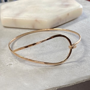 May include: A gold hammered metal bangle bracelet with a unique open oval design. The bracelet is simple and elegant, perfect for everyday wear.