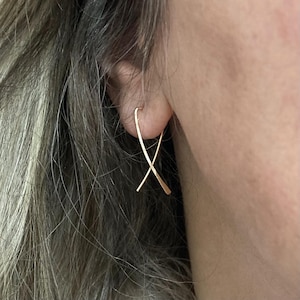 May include: Gold-toned, minimalist earrings with a simple, crossed line design. The earrings are made of a thin, delicate wire and are perfect for everyday wear.