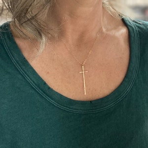 Pu&ograve; includere: Una collana d'oro con un ciondolo a forma di croce lungo e sottile.