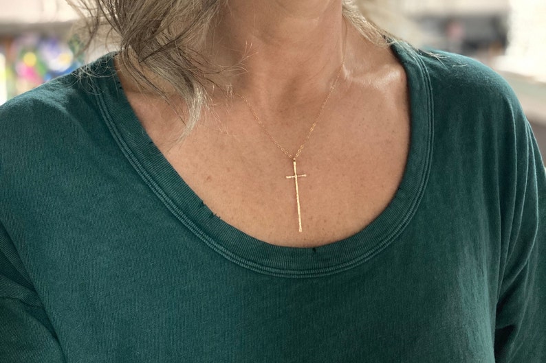 Pu&ograve; includere: Una collana d'oro con un ciondolo a forma di croce lungo e sottile.