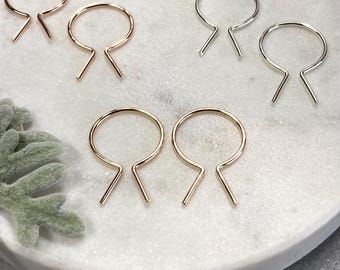 May include: Three pairs of hoop earrings in different finishes: gold, rose gold, and silver. Each pair has a unique design with a small, straight line extending from the hoop.