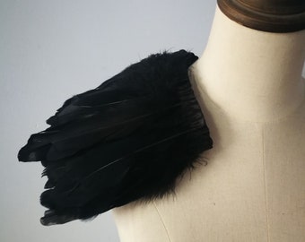 Könnte beinhalten: Schwarzes Federschulterstück für ein Kostüm oder ein Modeaccessoire. Die Federn sind in einer geschichteten, flügelartigen Form angeordnet.
