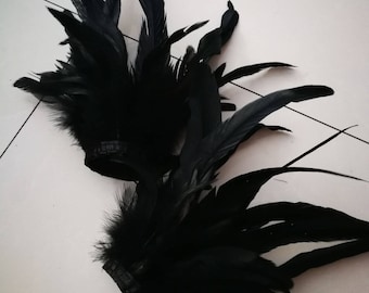 May include: Two clusters of black feathers, likely for crafting or costume design, are displayed against a white background. The feathers are dense and have a soft, textured appearance, with a dark, solid color.