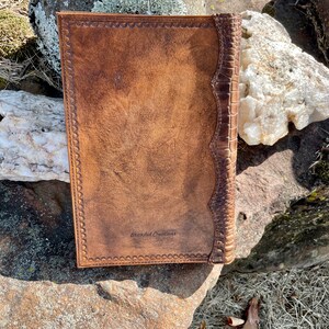May include: A brown leather journal with a decorative embossed border and a spine with a crocodile pattern. The journal has the text "Branded Creations" embossed on the front cover.